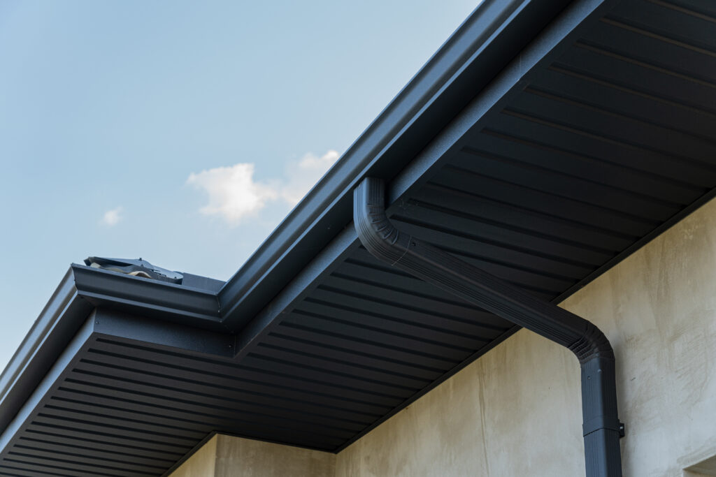 gutter downspouts Close view of a roof edge and downspout against a bright blue sky highlights contemporary construction features and materials.