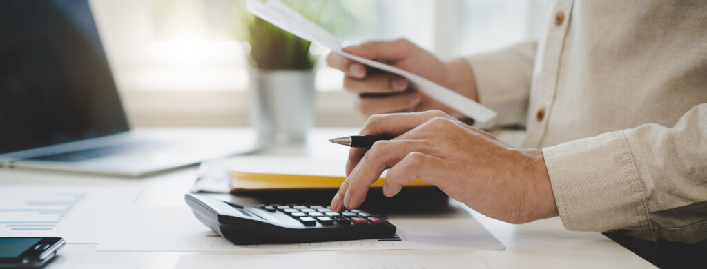 Deduction planning, debt asian accountant hand using calculator to calculating money balance from bill and income, cost budget expenses for pay money form personal individual on table at home.